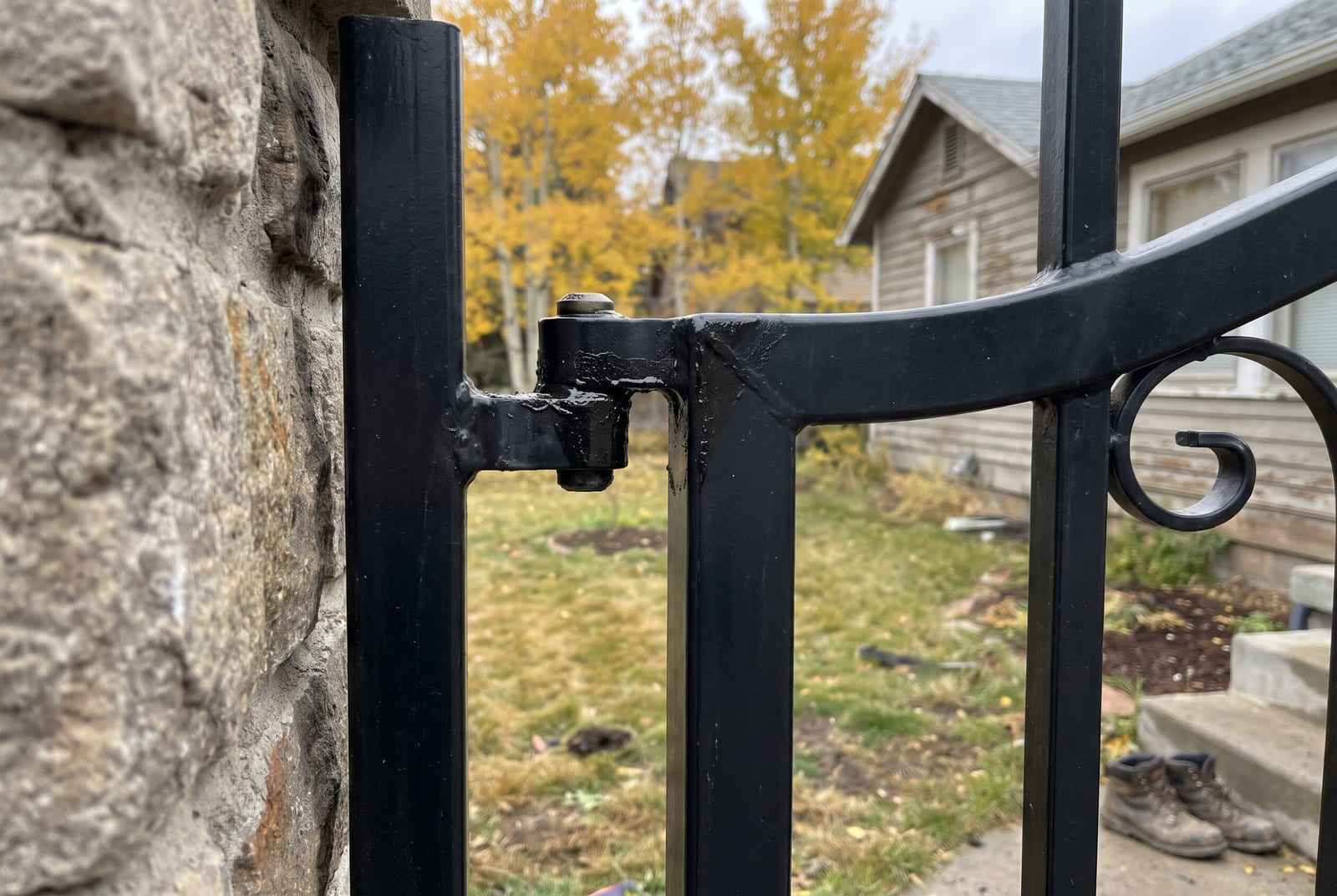 Freshly greased heavy hinges on a black wrought-iron driveway gate hung from a stone pier