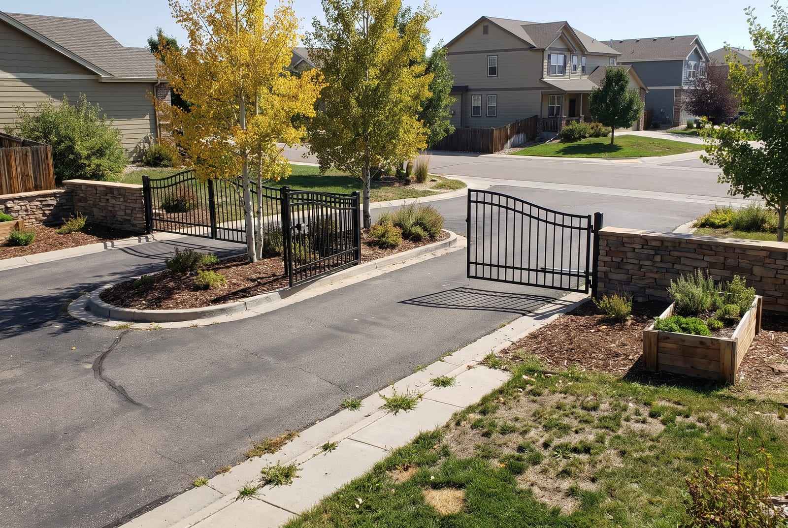 Pair of black wrought-iron swing gates standing open at the entrance of a residential neighborhood