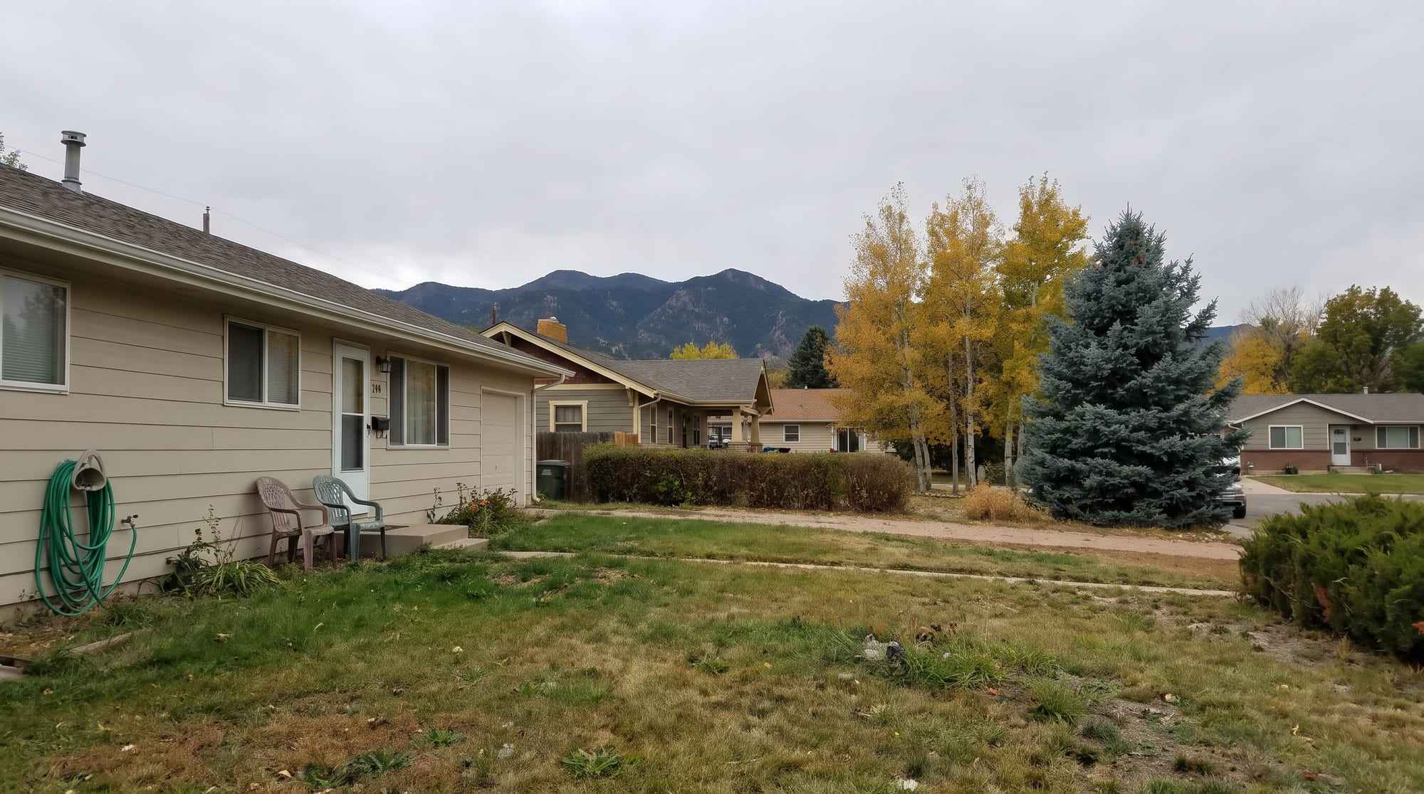 Front lawns of a quiet Colorado neighborhood with golden aspens, a blue spruce and mountains beyond the rooftops