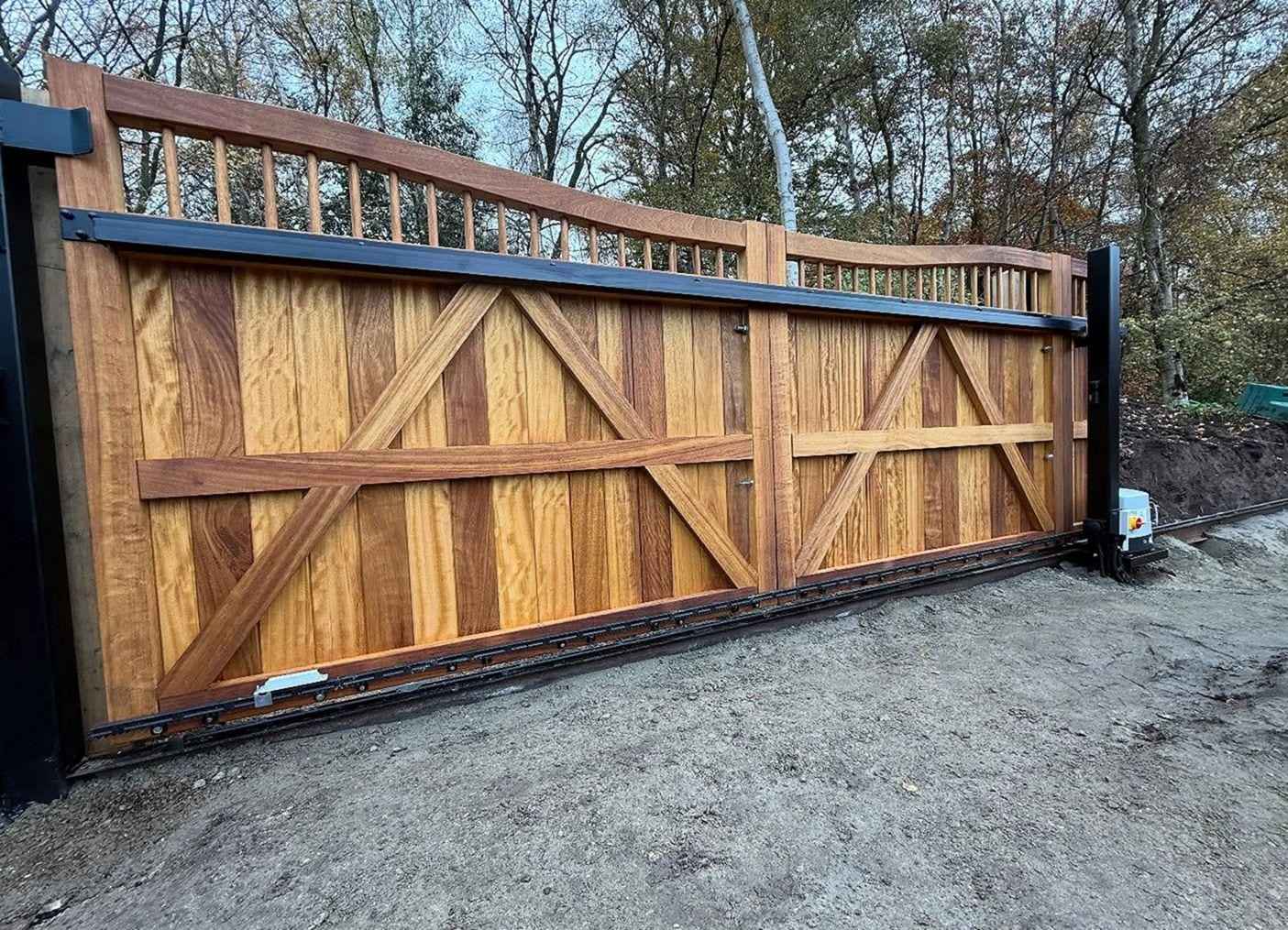 Hardwood sliding driveway gate with braced panels and a spindle top rail, the gear rack along its foot and the opener at the end of the run