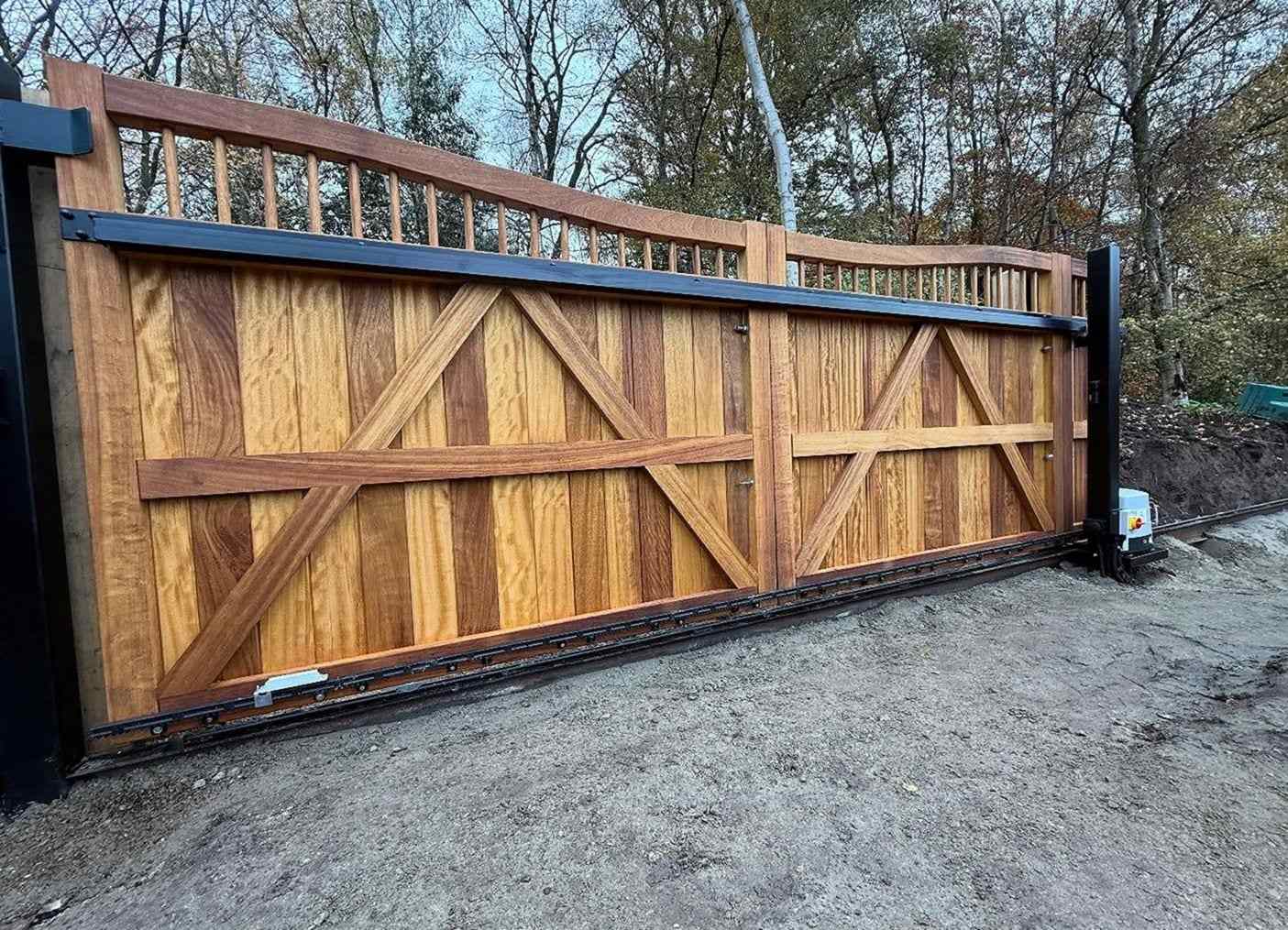 Hardwood sliding driveway gate with braced panels and a spindle top rail, the gear rack along its foot and the opener at the end of the run