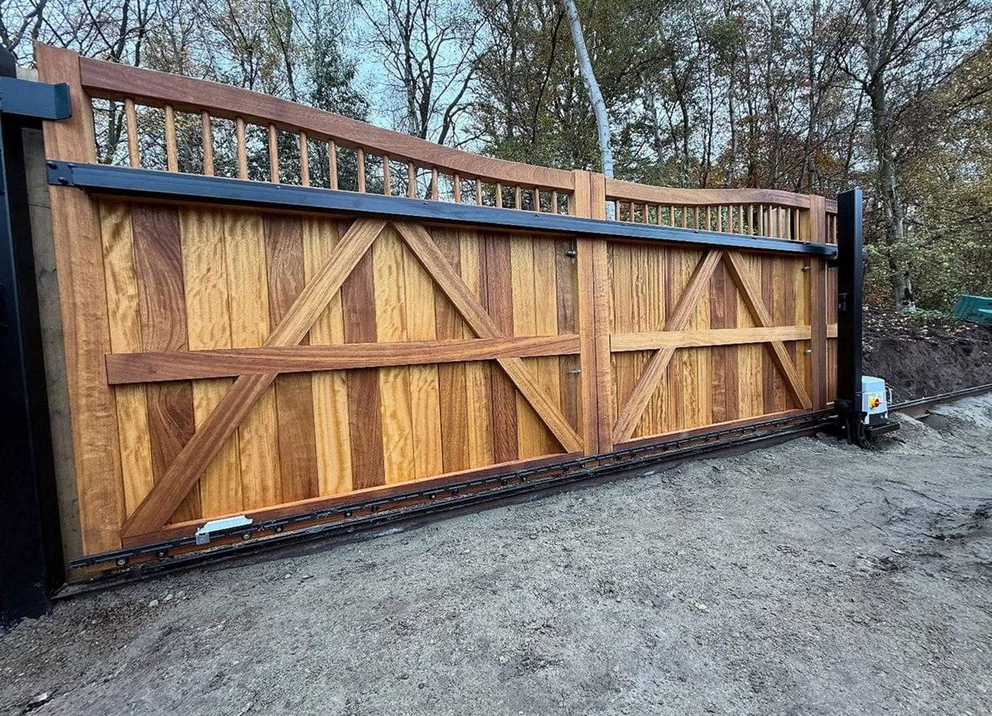 Hardwood sliding driveway gate with braced panels and a spindle top rail, the gear rack along its foot and the opener at the end of the run