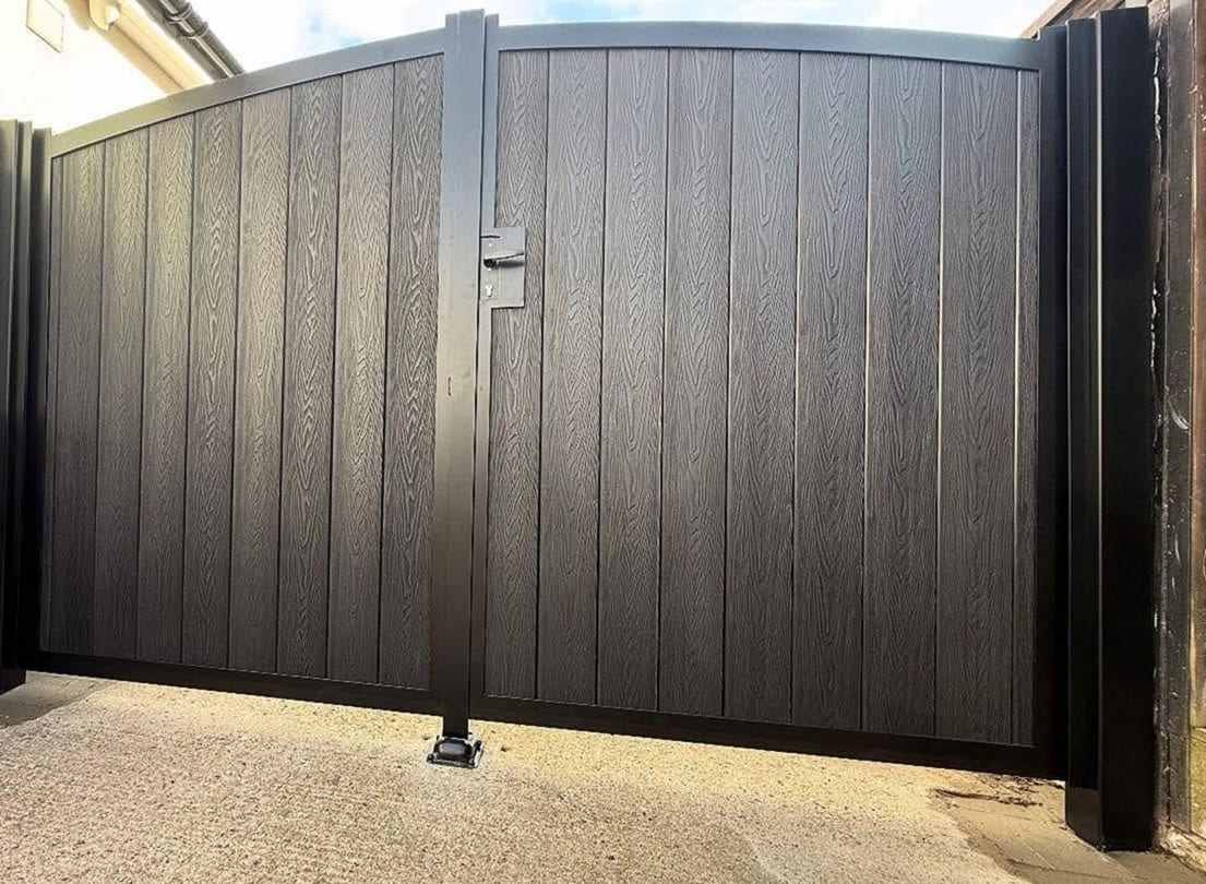 Pair of black composite swing gates with an arched top rail, a center latch and a drop bolt set into the concrete