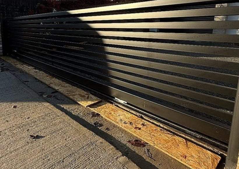 Horizontal-slat steel sliding gate on a freshly set ground track, protective boards still laid along the track