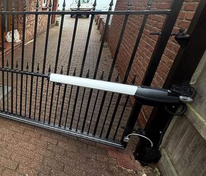 Linear ram opener arm fixed between a black railing swing gate and its steel hinge post